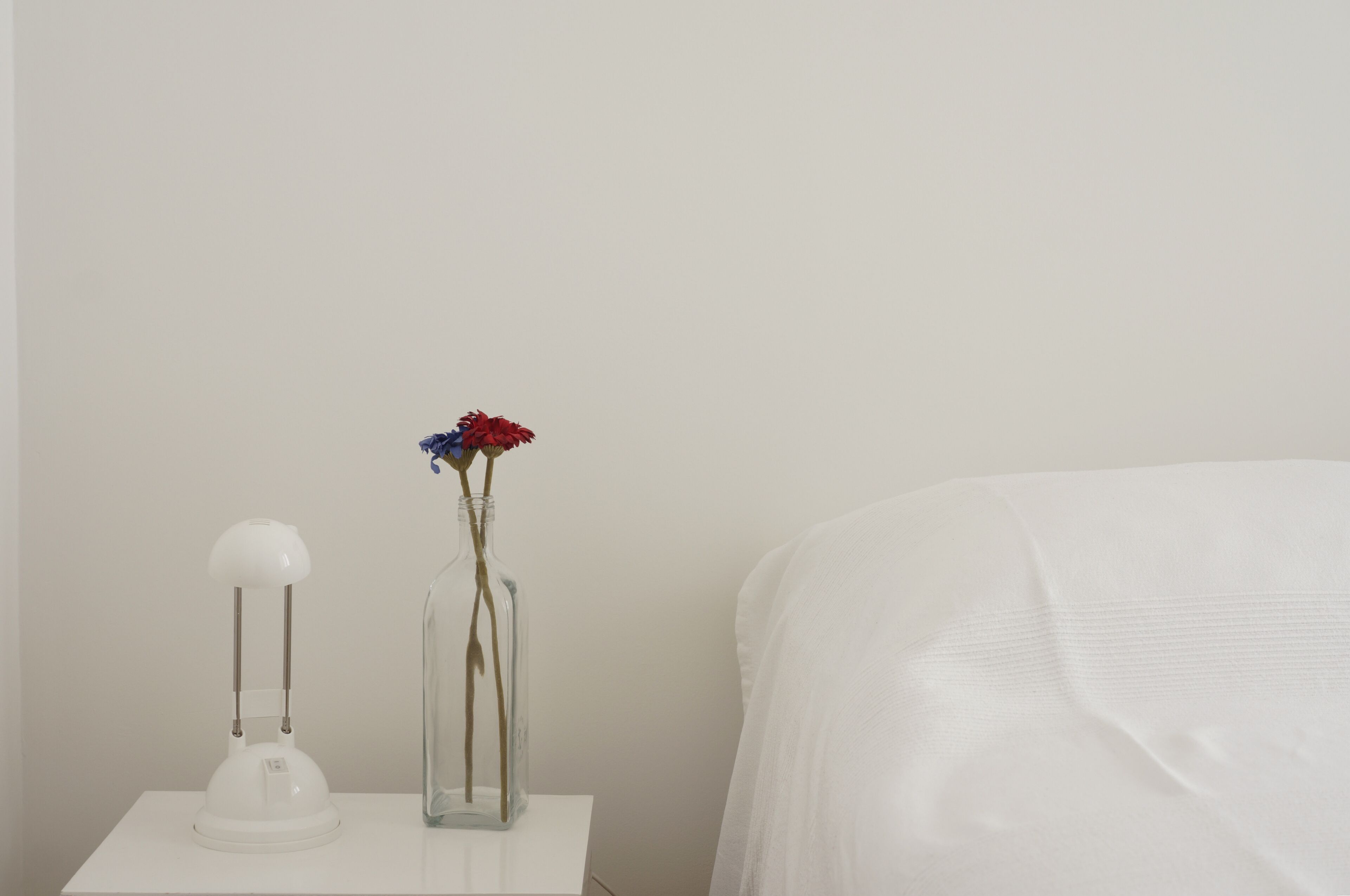 A white bedside table with a lamp and a vase containing flowers.