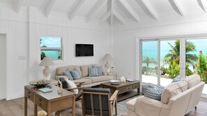A spacious living room with a large window offering a view of the ocean, a flat-screen TV mounted on the wall, and a cozy seating area with a sofa and armchairs. - Relaxation, Seclusion and Luxury -  beachfront and poolside (Little Exuma)