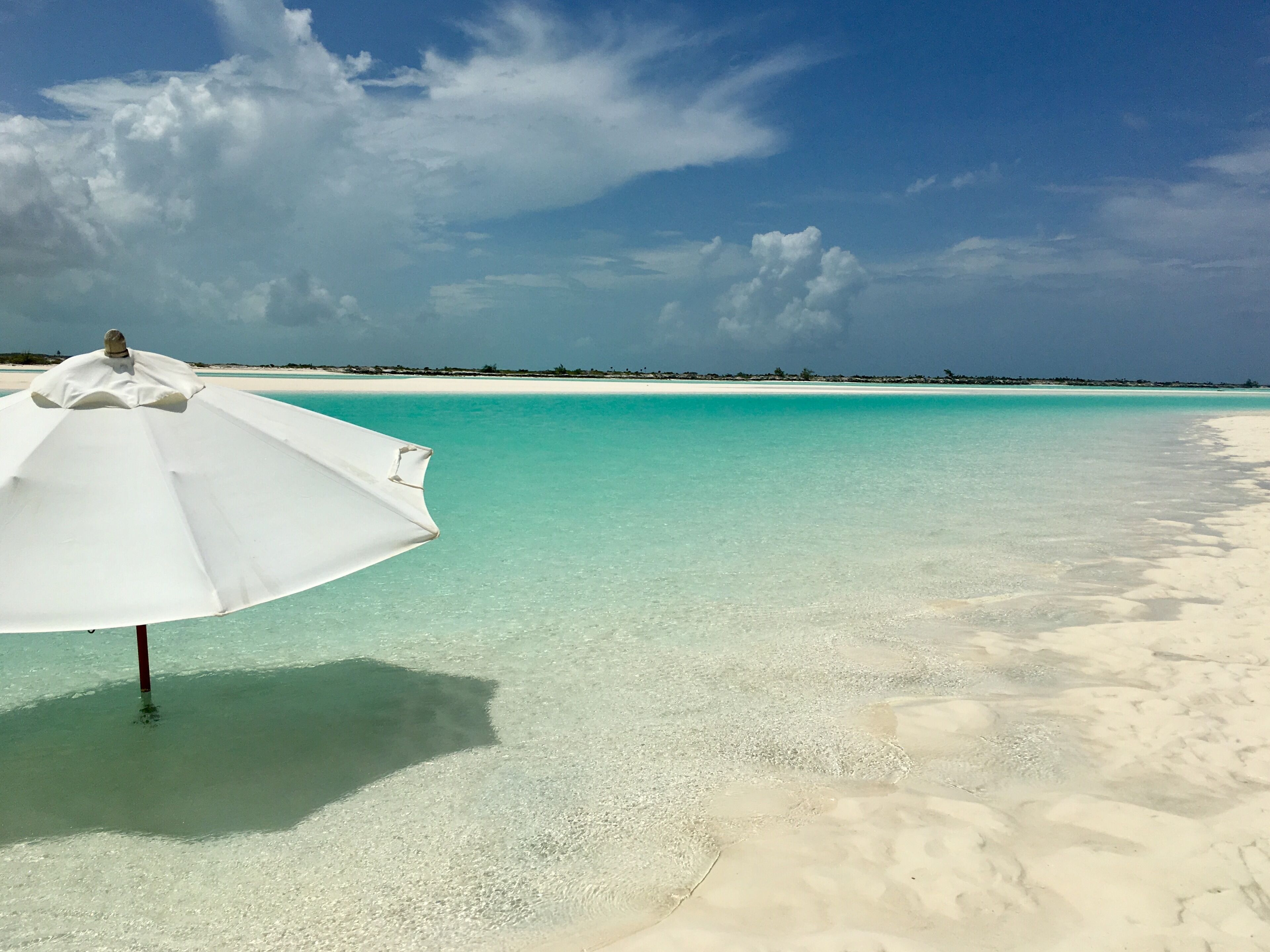 Una spiaggia con acque cristalline turchesi e un ombrellone bianco.