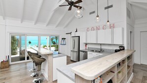 A modern kitchen with white cabinetry, a central island, and a view of the ocean. - Relaxation, Seclusion and Luxury -  beachfront and poolside (Little Exuma)