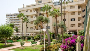 A multi-story hotel with balconies, palm trees, and a garden with benches and flowers. - PREMIUM 3 BEDROOMS PENTHOUSE BEACHFRONT IN TORREMOLINOS  (Torremolinos)