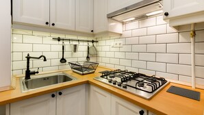 A modern kitchen with white cabinets, a stainless steel sink, a gas stove, and a hanging pot rack. - Kis Aldebaran Apartment: a little jewel in the center !! (Budapest)
