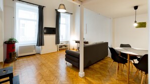 A modern living room with a herringbone wooden floor, a grey sofa, a dining table with chairs, and a black pendant light. - Kis Aldebaran Apartment: a little jewel in the center !! (Budapest)