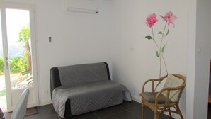 Una habitación con un sofá gris, un sillón de mimbre y un aire acondicionado instalado en la pared.