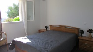 Un dormitorio con cama, mesita de noche, silla, ventana con cortinas y lámpara colgante.