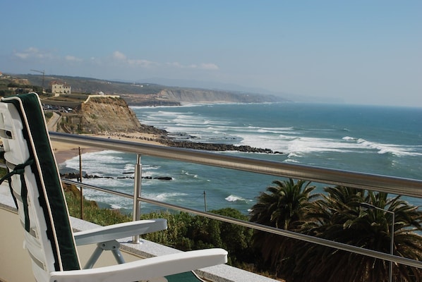 Vista al mar desde un balcón con barandilla, que domina una costa rocosa y el océano.