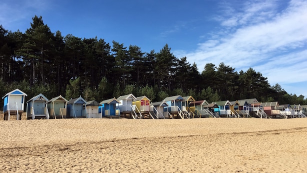 A row of beach huts with a sandy beach and forest in the background.