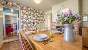 A dining area with a wooden table set for four, a vase of flowers, and a brick wall with a floral pattern.
