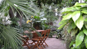 Een terras met een houten tafel en stoelen, omringd door weelderige begroeiing en planten.