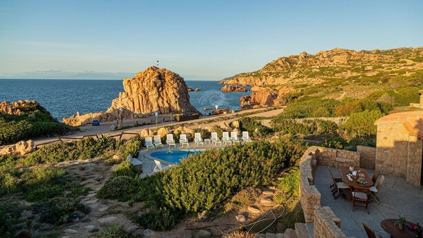 A coastal resort with a swimming pool, lounge chairs, and a stone patio. - Villa Sfumature del Melograno: private pool in front of the sea (Costa Paradiso)