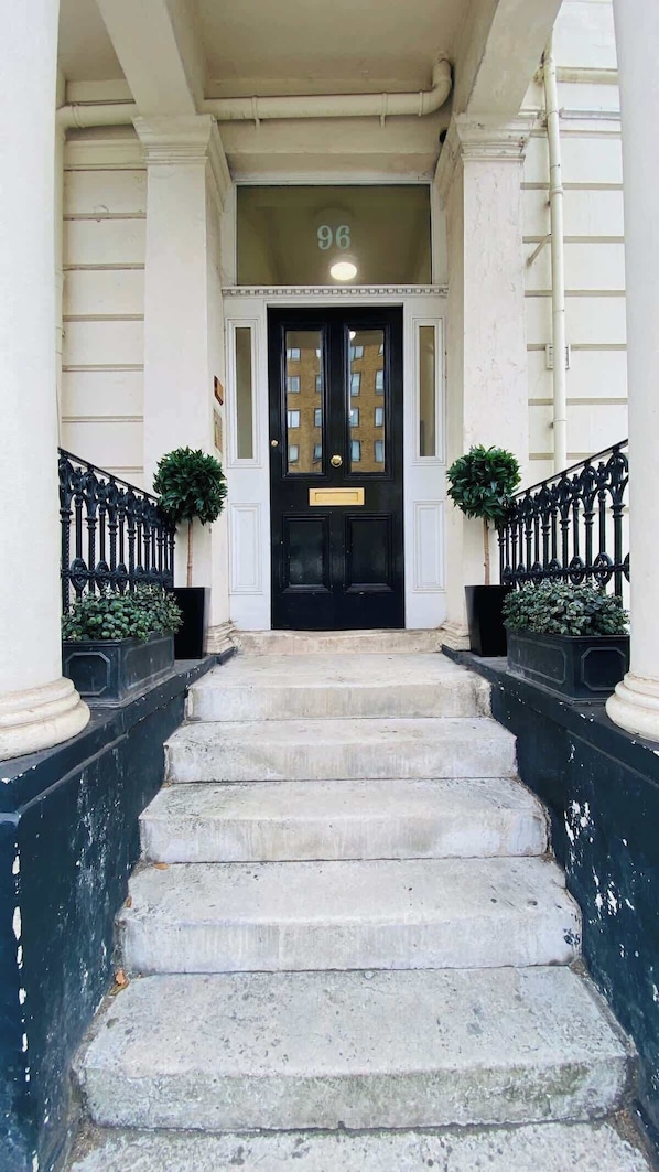 A grand entrance with a black door, white columns, and a number '96' above the door.