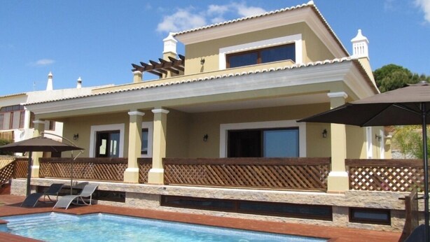 A two-story house with a swimming pool, outdoor seating, and a pergola.