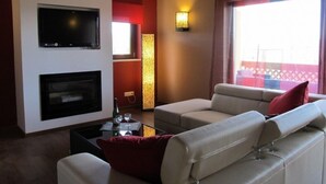A living room with a flat-screen TV, a fireplace, a sofa, and a table with glasses and a bottle.