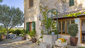 Un bâtiment en pierre avec des volets verts, des plantes en pot et un banc en pierre.