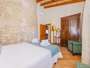 Una habitación de hotel con una cama, un armario de madera, un sillón verde y una mesita de noche con una lámpara.