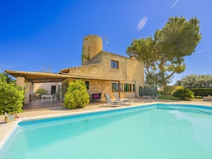 Un edificio de piedra con piscina, mobiliario exterior y un gran árbol.