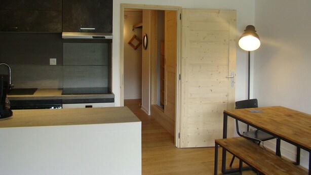 Eine moderne Küche mit dunklen Schränken, einer Holztür und einem Essbereich mit Tisch und Bank.