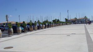 Une vaste place en béton, ouverte et dégagée, bordée de rangées de jardinières cylindriques, et surplombée d’un ciel d’un bleu éclatant.
