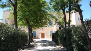 Un chemin menant à un bâtiment doté d’une porte centrale, bordé d’arbres et d’arbustes.