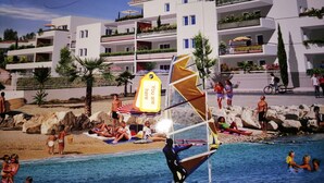 A beach scene with a swimming pool, people sunbathing, and a sailboat. - Beachside sea views, aircon, internet, modern, private parking (Mèze)