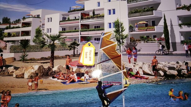 Une scène de plage avec une piscine, des gens qui prennent un bain de soleil et un voilier.