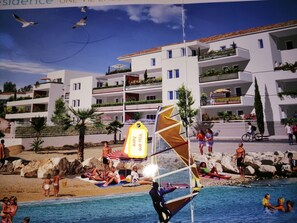 A beach scene with a swimming pool, people sunbathing, and a sailboat.