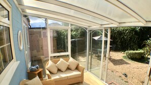 A conservatory with a wicker sofa, a small table, and a chair. - Pretty Thatched Cottage, close to sandy beach (winterton on sea)