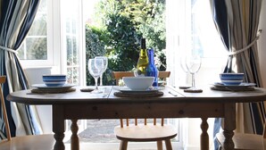 A dining table with a bottle, bowls, and glasses, set against a window with curtains. - Pretty Thatched Cottage, close to sandy beach (winterton on sea)