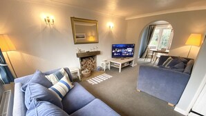 A living room with a sofa, a television, a fireplace, and a dining area. - Pretty Thatched Cottage, close to sandy beach (winterton on sea)