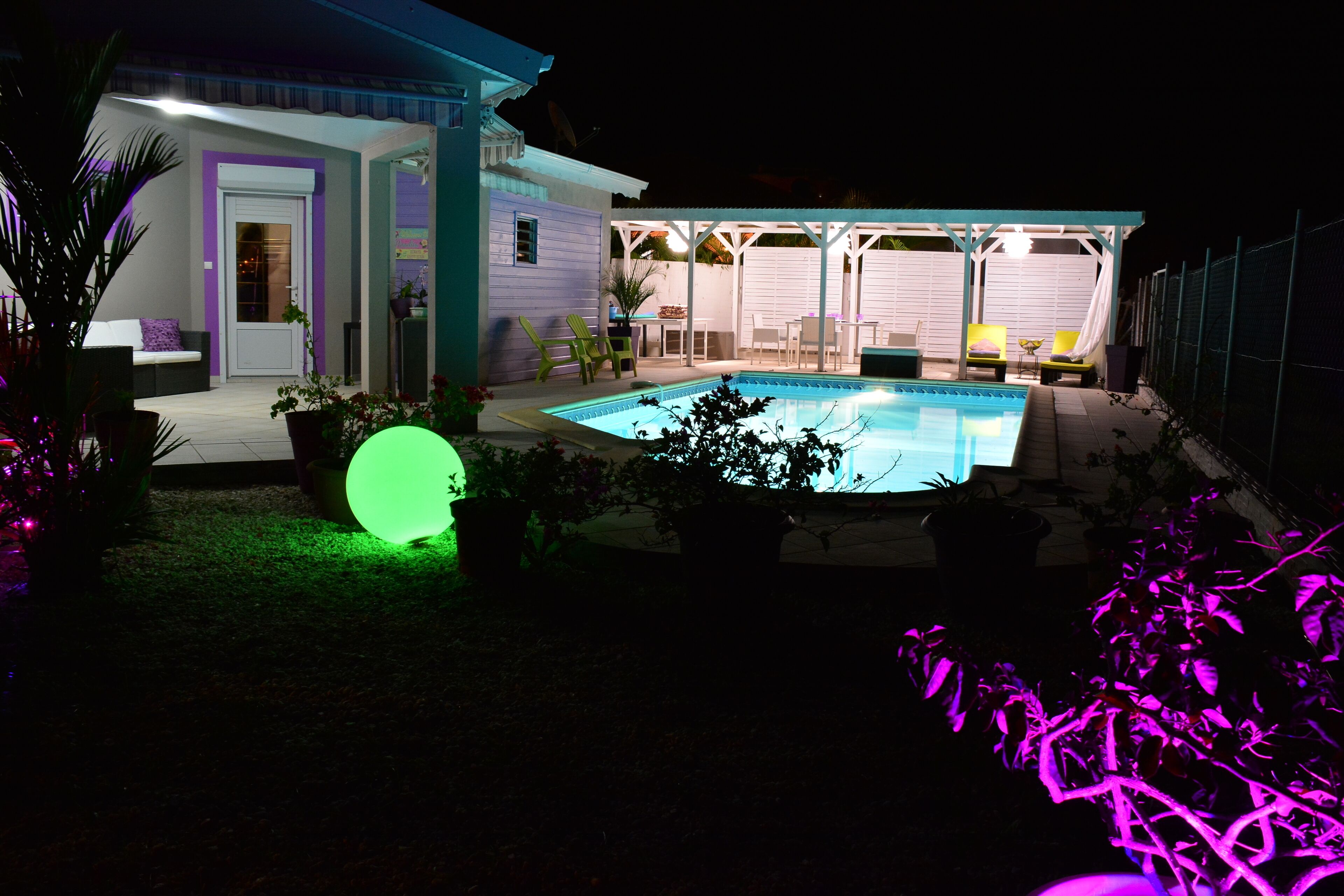 A backyard with a swimming pool, a covered patio area, and a house with a door and windows.