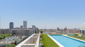 Una piscina en la azotea con vista a la ciudad, rodeada de vegetación y edificios modernos.
