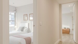 Ein Schlafzimmer mit einem Bett, Nachttischen, einem Fenster und einer Tür zu einem anderen Raum.