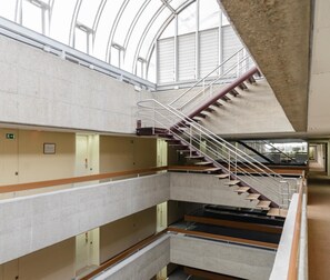 Un interior de varios niveles con una escalera central, señales de salida de emergencia y un techo de cristal.