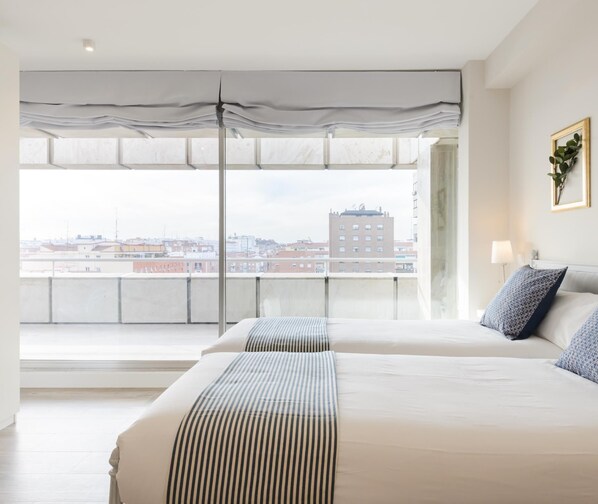 Una habitación de hotel moderna con dos camas, ventanas amplias y vista a la ciudad.