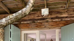 A rustic wooden cabin with a stone wall, a bed with a white headboard, and a hanging light fixture.