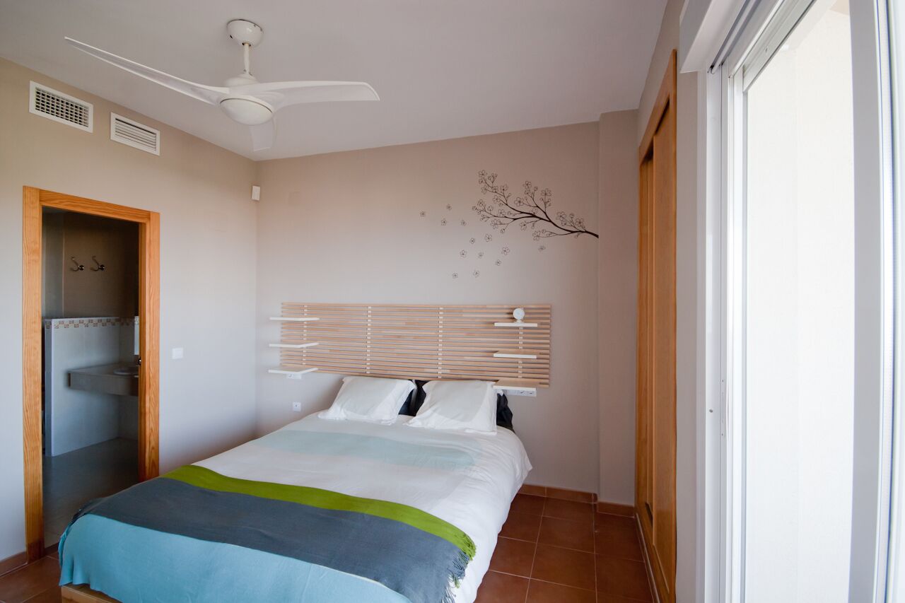 A bedroom with a bed, a ceiling fan, a window, and a wall decoration.