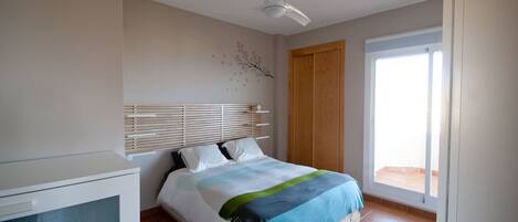 A bedroom with a bed, a ceiling fan, a wooden door, and a window.