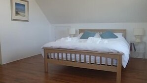 A bedroom with a wooden bed, white bedding, and a picture on the wall. - Contemporary Beach House with sea views and short walk to Blue Flag beach (Porthtowan)