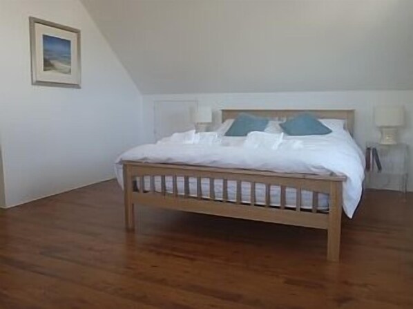 A bedroom with a wooden bed, white bedding, and a picture on the wall.