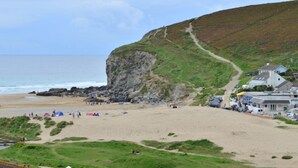 A coastal area with a sandy beach, a cliff, and a path leading up to a building. - Contemporary Beach House with sea views and short walk to Blue Flag beach (Porthtowan)