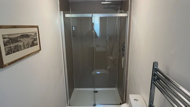 A compact bathroom with a glass-enclosed shower, a toilet, and a framed picture on the wall. - Contemporary Beach House with sea views and short walk to Blue Flag beach (Porthtowan)