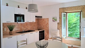 A modern kitchen with white cabinets, a black countertop, and a window with a view of greenery. - Near the sea , the quiet and the charm of " LA  FORGE" (Narbonne)