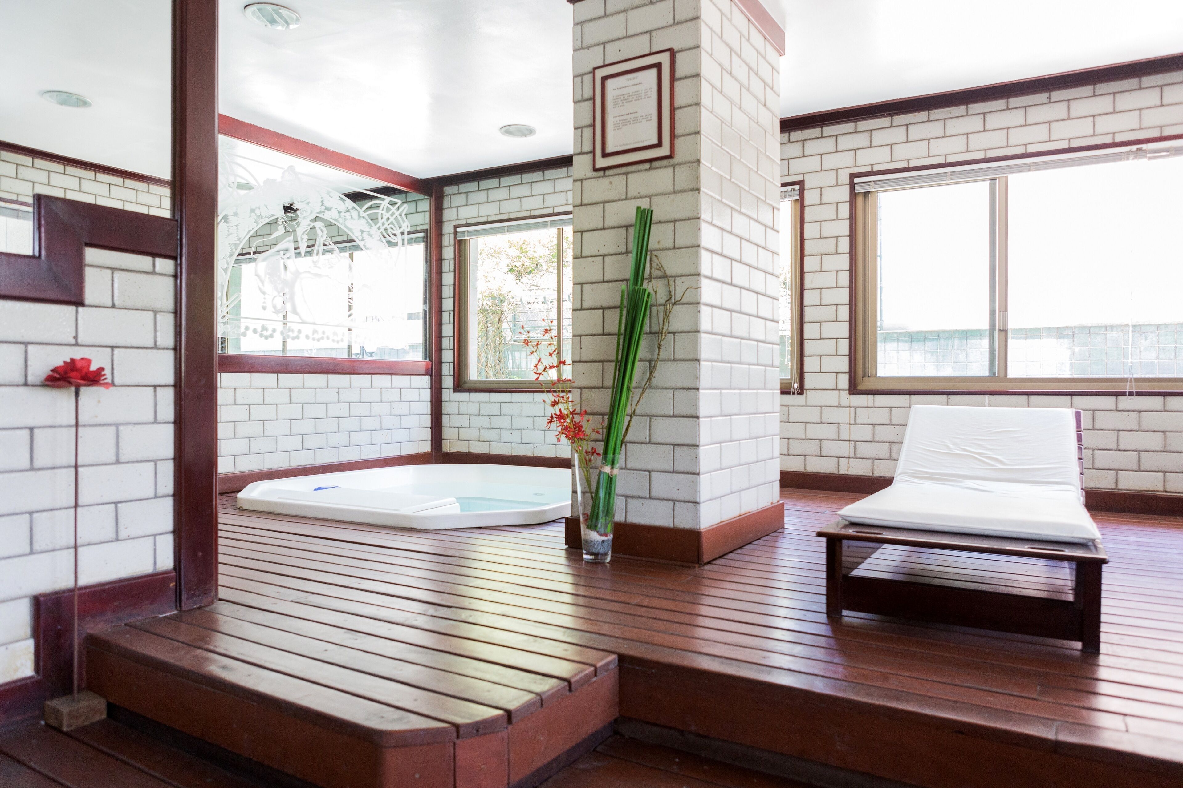 Un espace de bien-être doté d’une terrasse en bois, d’un jacuzzi, d’une table de massage et d’un vase rempli de fleurs.