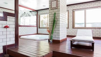Un espace de bien-être doté d’une terrasse en bois, d’un jacuzzi, d’une table de massage et d’un vase rempli de fleurs.