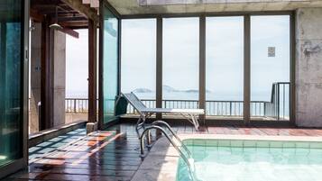 Área da piscina com vista para o mar, uma espreguiçadeira e uma mesa pequena.