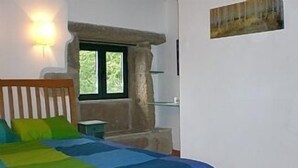 Ein Schlafzimmer mit einem Bett, einem Nachttisch, einer Lampe, einem Fenster und einem Gemälde an der Wand.