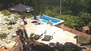 Ein Pool mit Liegestühlen und einem Sonnenschirm, umgeben von einer Steinmauer und viel Grün.