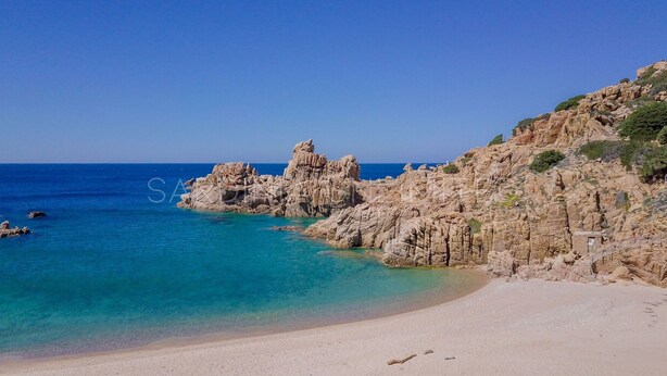 Paisatge costaner amb penya-segades rocoses, aigües turqueses cristal·lines i una platja de sorra.