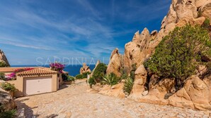Un camí pavimentat de pedra que condueix a un edifici amb porta de garatge, envoltat de terreny rocos i vegetació escassa.