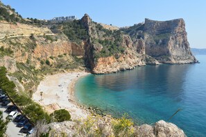 Eine Küstenlandschaft mit einer felsigen Klippe, einem Strand und einem tiefblauen Meer.